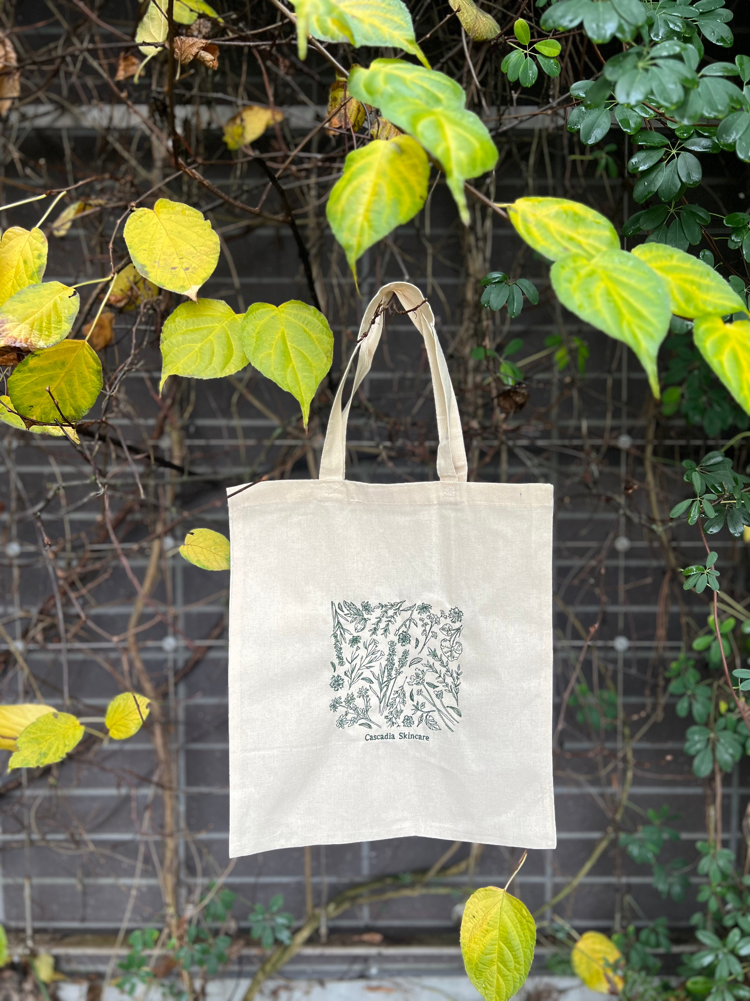 Tote bag with floral embroidered design hanging against a leafy background