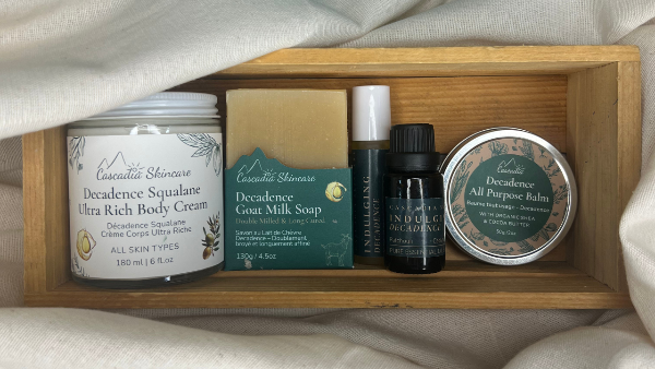 Set of Decadence skincare and body care products in a wooden box on a textured fabric background