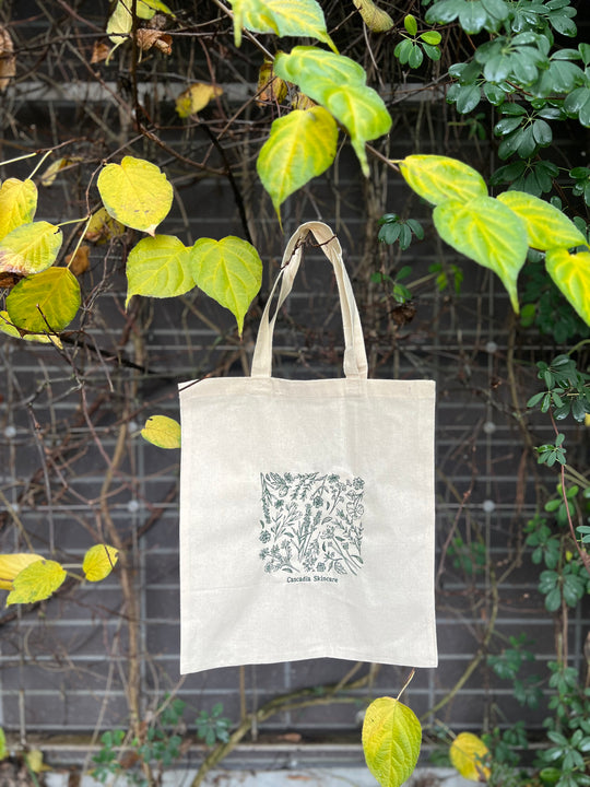 Tote bag with floral embroidered design hanging against a leafy background