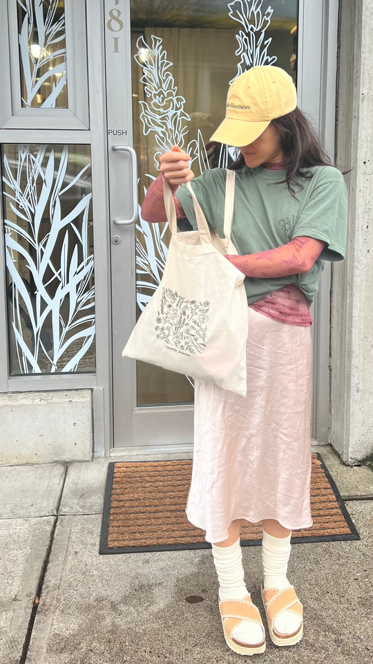 Woman standing outside the Cascadia Skincare store holding the Cascadia Floral Embroidery tote bag.
