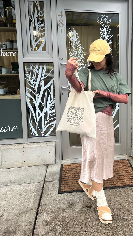 Person wearing a yellow cap and green shirt, holding a Cascadia Floral Embroidery tote bag with a building in the background