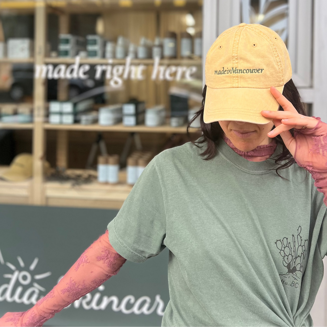Person wearing the Cascadia Made in Vancouver yellow cap and green t-shirt in front of a store with 'made right here' sign.