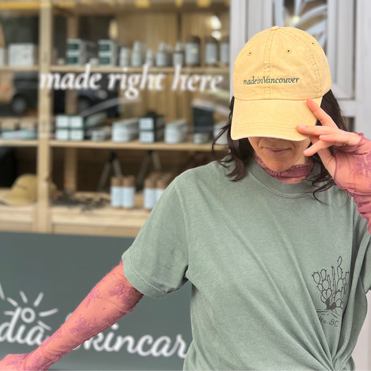 Person wearing the Cascadia Made in Vancouver yellow cap and green t-shirt in front of a store with 'made right here' sign.
