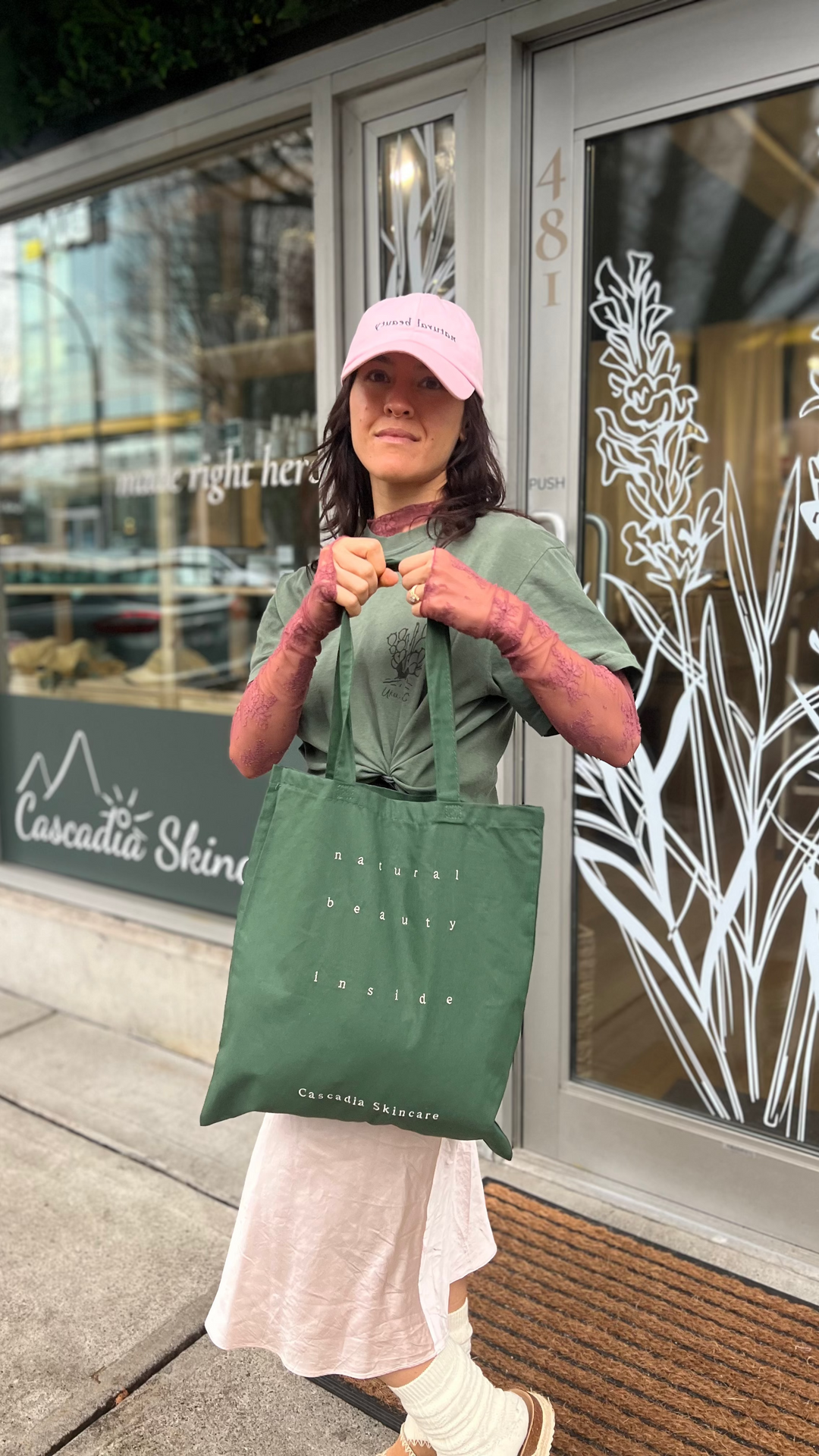 Woman holding the Cascadia natural beauty inside green tote bag and wearing the Cascadia natural beauty hat.