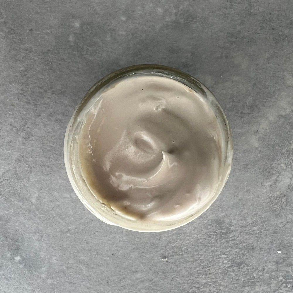 Glass container with a swirl of Cascadia Botanical Eye Cream on a gray surface