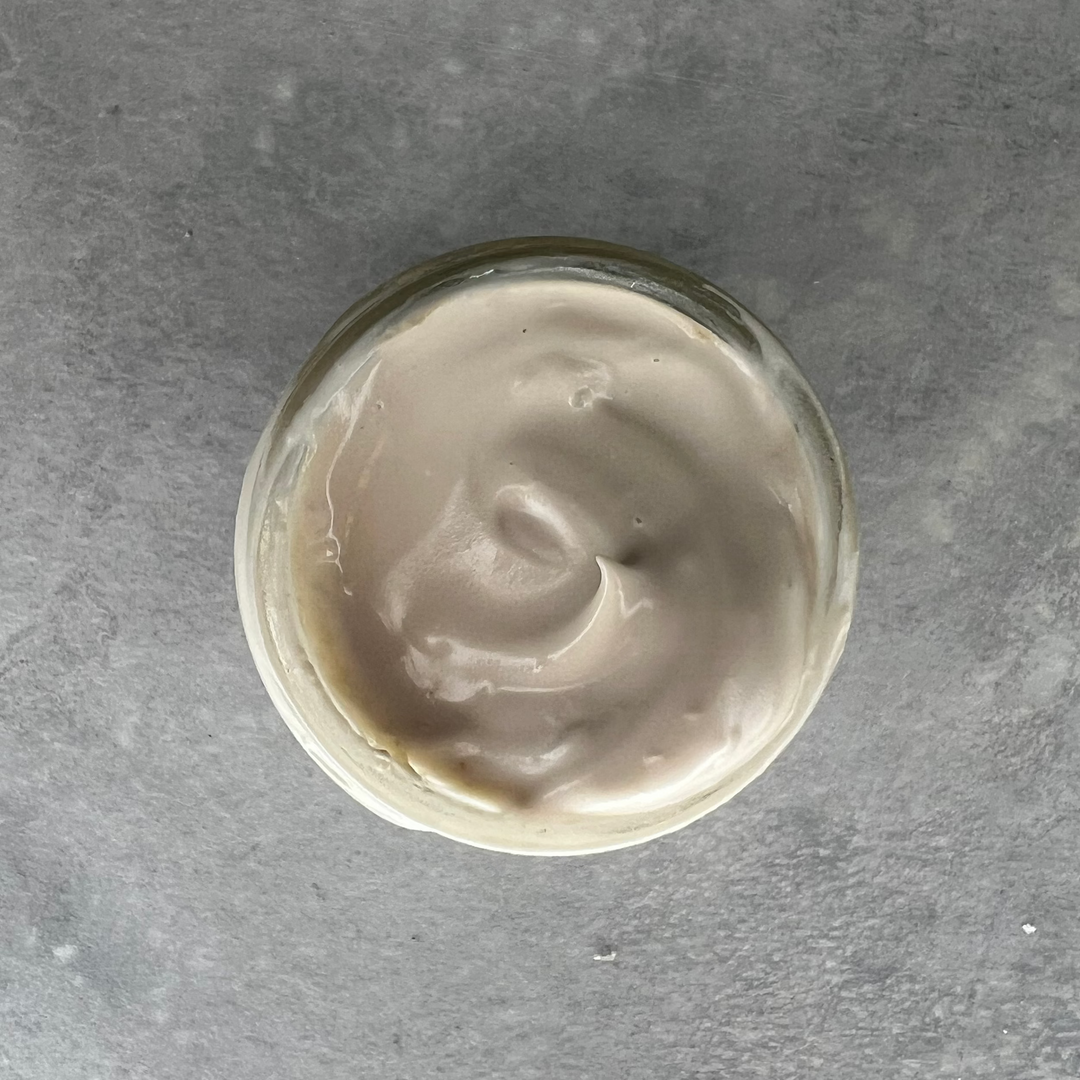 Glass container with a swirl of Cascadia Botanical Eye Cream on a gray surface