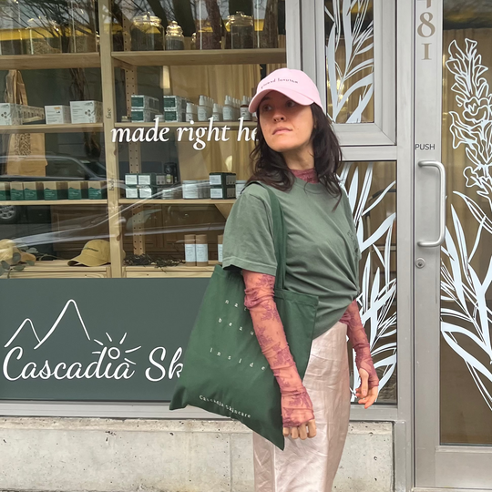 Woman standing outside a building with the Cascadia natural beauty cap and the Cascadia natural beauty inside tote.